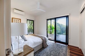 A bedroom with a bed, a bedside table, a window, and a door leading to an outdoor balcony. - Dogs welcome @ Beachside Beauty - 31 Tristania Drive (Noosa)