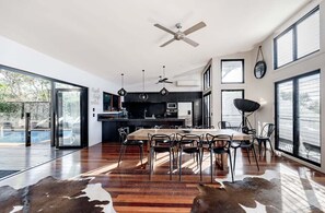 A modern kitchen with a dining area, large windows, and a ceiling fan. - Dogs welcome @ Beachside Beauty - 31 Tristania Drive (Noosa)
