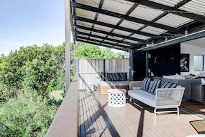 An outdoor deck with a sofa, two side tables, and a wicker chair. - Dogs welcome @ Beachside Beauty - 31 Tristania Drive (Noosa)