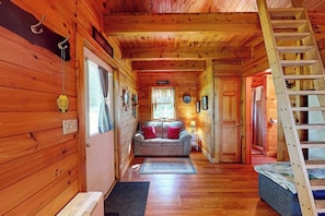 Ein Holzblockhaus-Interieur mit Holzboden, einer Couch, einer Leiter und einer Tür zu einem anderen Raum.
