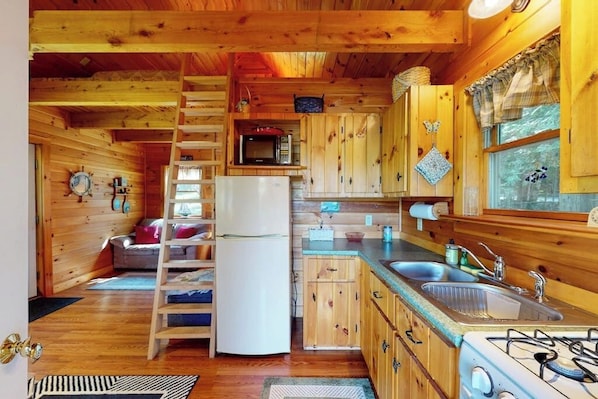 Ein Holzblockhaus-Interieur mit Küche, inklusive Kühlschrank, Mikrowelle, Spüle und Herd.