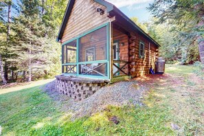Eine Blockhütte mit Glasfront, einer Steintreppe und einem Kiesweg.