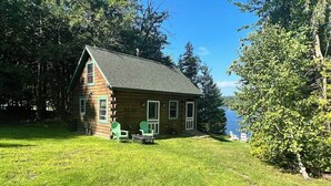 A log cabin with a grassy yard, a small deck, and a view of a lake.