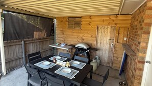 En uteplats med ett bord dukat för måltider, en grill och en mur av tegelsten.