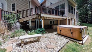 Una casa de dos pisos con un porche cubierto, un jacuzzi y un camino de piedra.