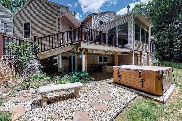 A two-story house with a covered patio, a hot tub, and a stone pathway.
