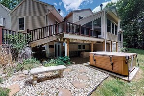 A two-story house with a covered patio, a hot tub, and a stone pathway.