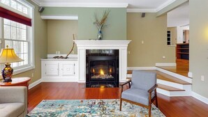Una sala de estar con chimenea, suelo de madera, un sofá, una silla y una alfombra.