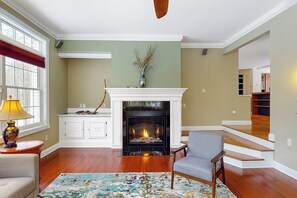 A living room with a fireplace, wooden flooring, a sofa, a chair, and a rug.