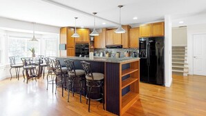 Una cocina moderna con armarios de madera, una isla central con taburetes de bar, iluminación colgante y un refrigerador de acero inoxidable.