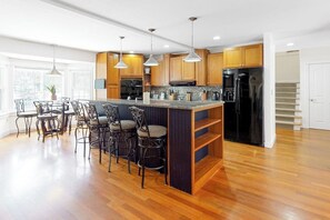 A modern kitchen with wooden cabinets, a central island with bar stools, pendant lighting, and a stainless steel refrigerator.