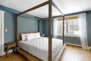 A four-poster bed in a room with teal walls, wooden flooring, and a window with white curtains.