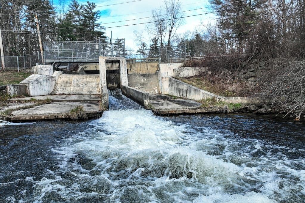 A concrete water control structure with a gated entrance over a turbulent river.
