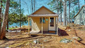 A small cabin with a porch, surrounded by trees and a lake. - Refurbished waterfront 1950s cabin with sauna, firepit, grill & kayaks - dogs ok (Raymond)