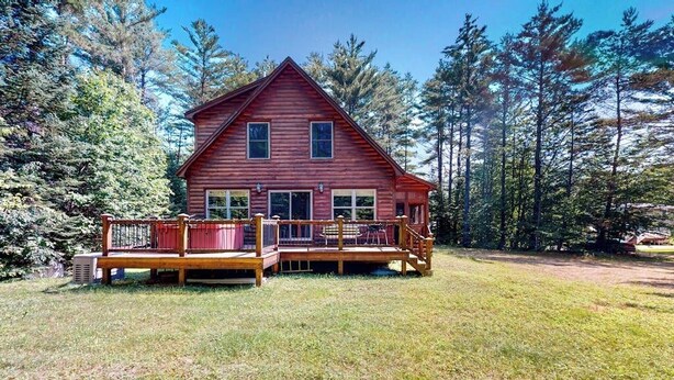 A two-story log cabin with a deck, surrounded by a forest. - Log cabin 1 mile from Sunday River with hot tub, fireplace & Ping-Pong (Newry)