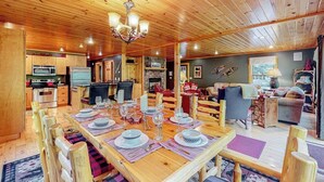 A wooden interior with a dining table set for four, a kitchen with appliances, and a living area with seating. - Log cabin 1 mile from Sunday River with hot tub, fireplace & Ping-Pong (Newry)