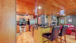 A kitchen with wooden cabinets, a microwave, a refrigerator, and a bar area with stools. - Log cabin 1 mile from Sunday River with hot tub, fireplace & Ping-Pong (Newry)
