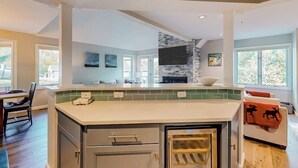 Eine moderne Küche mit Kochinsel, ein Essbereich mit Tisch und Stühlen sowie ein Wohnbereich mit Sofa und Kamin.