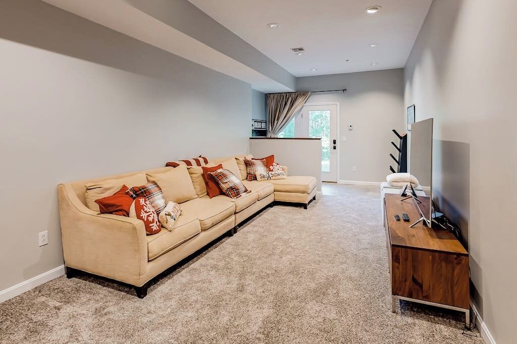 A living room with a beige sectional sofa, a wooden TV stand, and a door leading to a balcony.