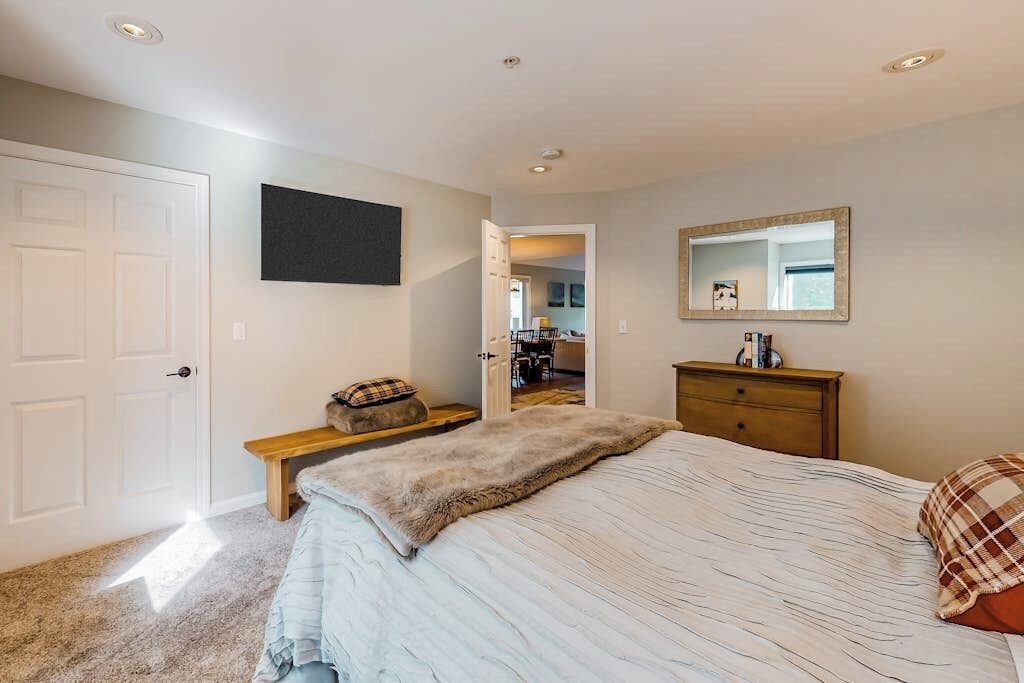 A bedroom with a bed, a bench, a dresser, a mirror, and a door.
