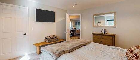 A bedroom with a bed, a bench, a dresser, a mirror, and a door.