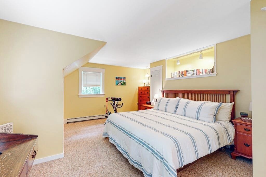 Un dormitorio con cama, mesita de noche, cómoda, ventana y estantería.