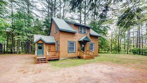 Een houten chalet met twee verdiepingen en een veranda, omringd door een bos.