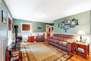 A living room with a sofa, a coffee table, a TV stand, and a wall decorated with framed photos. - Sheridans' Getaway | Dog-friendly house in Newry, 1 mile to Sunday River (Newry)