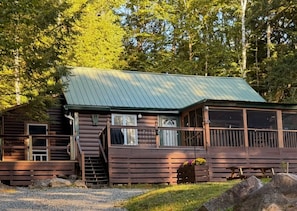 Une cabane rustique avec un toit en métal, une terrasse en bois et un escalier menant à l’entrée.