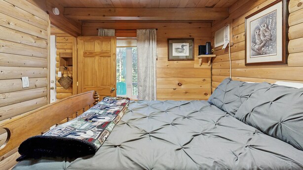 A wooden cabin interior with a bed, a door, a window, and a shelf with framed pictures. - Charming Lakeview House with Deck, Cozy Fireplace and firepit (Rome)
