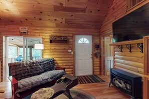 A log cabin interior with a sofa, a fireplace, a door, and a welcome sign. - Charming Lakeview House with Deck, Cozy Fireplace and firepit (Rome)
