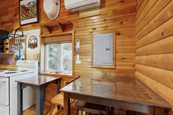 Interior de una cabaña de madera con cocina, que incluye estufa, mesa y sillas.