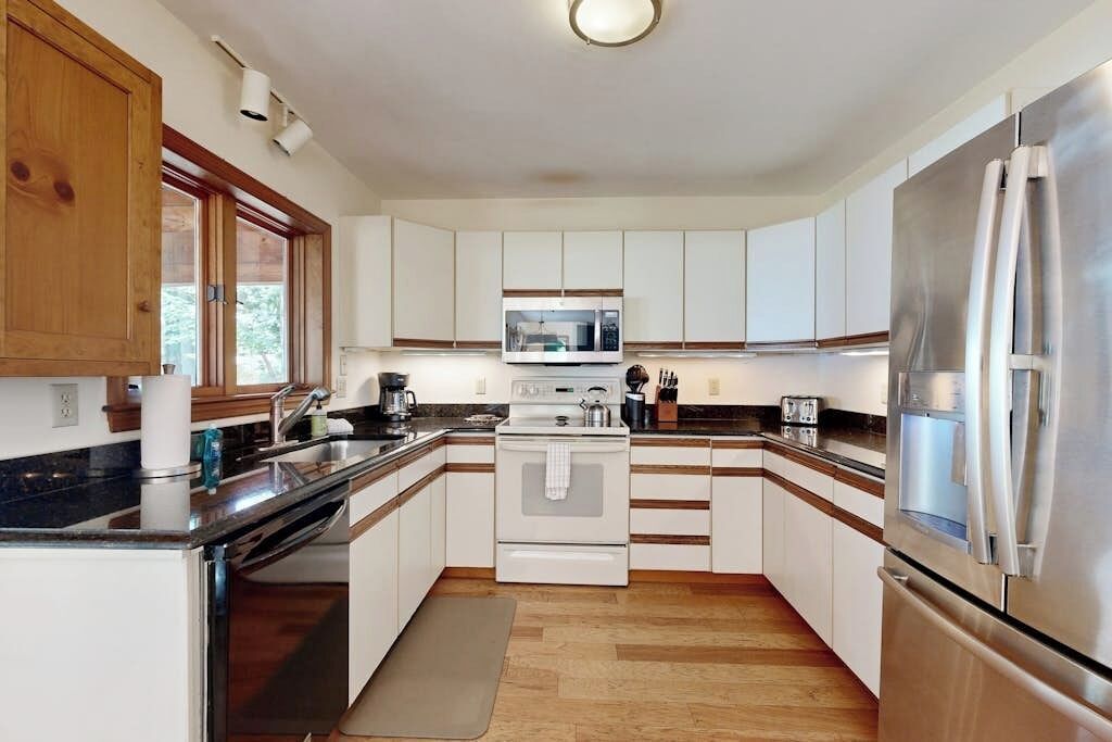 Une cuisine moderne avec des meubles blancs, des appareils en acier inoxydable et un plancher en bois.