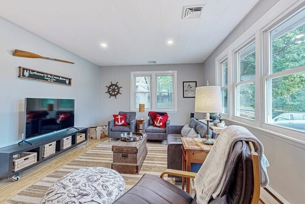 A living room with a TV, sofas, a coffee table, and a large window. - Charming Retreat House with Game room and Outdoor Firepit (Naples)