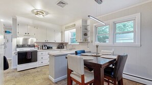 Een keuken met witte kasten, een fornuis, een spoelbak en een eethoek met een tafel en stoelen.
