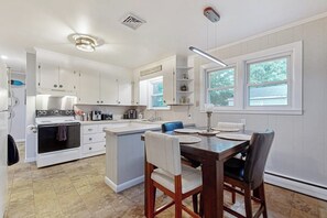 A kitchen with white cabinets, a stove, a sink, and a dining area with a table and chairs. - Charming Retreat House with Game room and Outdoor Firepit (Naples)