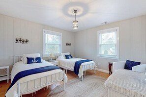 A bedroom with two beds, a white wicker chair, and a white sofa. - Charming Retreat House with Game room and Outdoor Firepit (Naples)