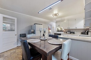 A modern kitchen with white cabinets, a dining table with placemats, and a built-in island with a sink. - Charming Retreat House with Game room and Outdoor Firepit (Naples)