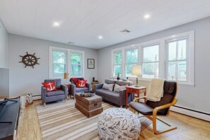 A spacious living room with large windows, a wooden floor, and a cozy seating area. - Charming Retreat House with Game room and Outdoor Firepit (Naples)