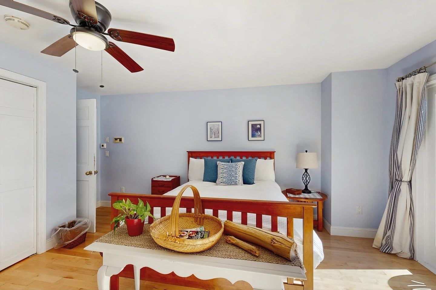 A bedroom with a bed, bedside tables, a ceiling fan, a window with curtains, and a door.