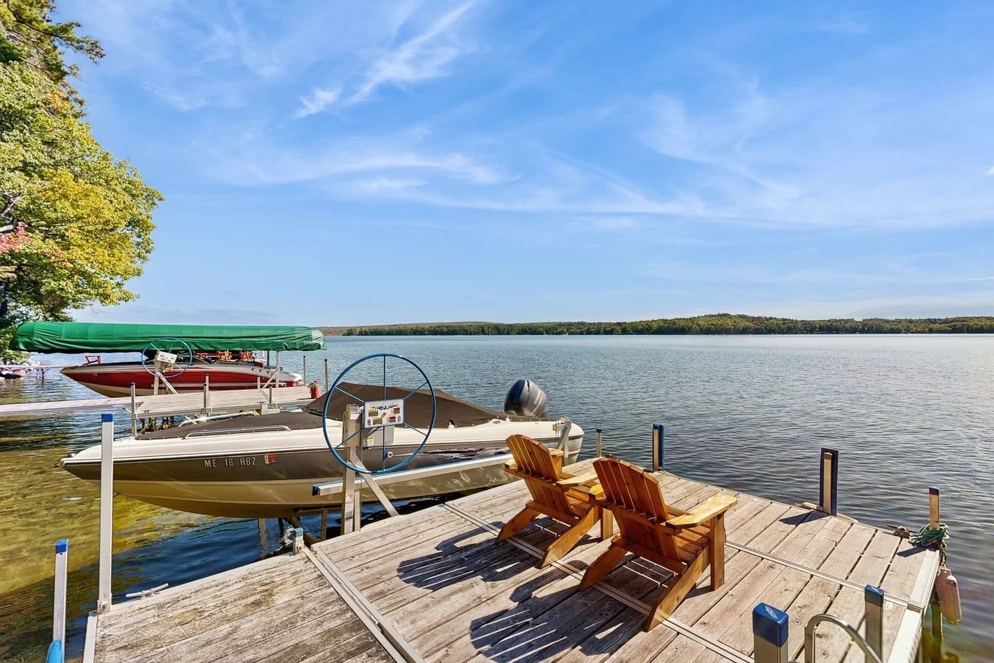 A wooden dock with two lounge chairs, a boat, and a green canopy.