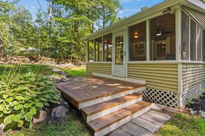Ein Haus mit einer Veranda, einem kleinen Deck und einer Holztreppe zum Eingang.