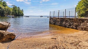 A beach with a stone wall, clear water, and boats.