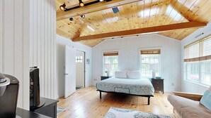Quarto com cama, televisão, teto de madeira e janelas grandes.