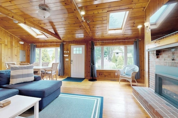 A wooden cabin interior with a sofa, dining table, and fireplace. - Charming home with patio & studio - walk to Footbridge Beach (Ogunquit)