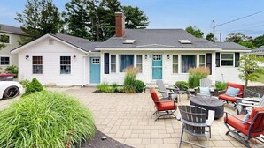 Uma casa de dois andares com um pátio com móveis de exterior e uma lareira.
