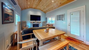 A room with a wooden ceiling, a television, a fireplace, a dining table, and a door with a window.