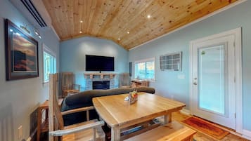A room with a wooden ceiling, a television, a fireplace, a dining table, and a door with a window.
