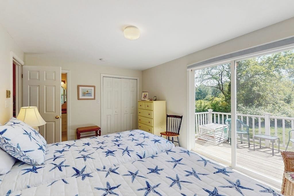 Un dormitorio con cama, una silla, un aparador y una puerta que da a otra habitación.