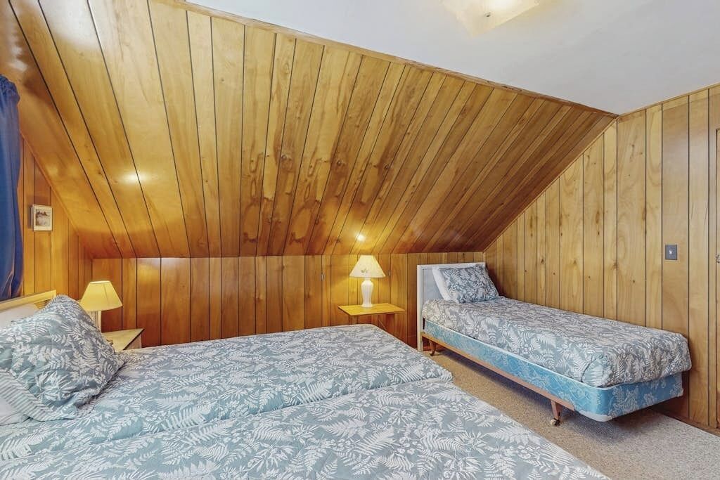 Een kamer met houten lambrisering, twee bedden met beddengoed met een patroon, een nachtkastje met een lamp en een plafondlamp.